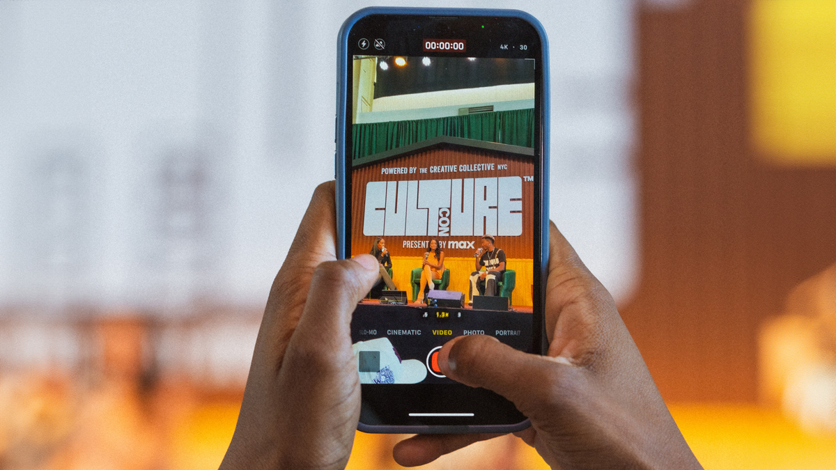 Photo of hands holding a mobile phone capturing a Culture Con panel.