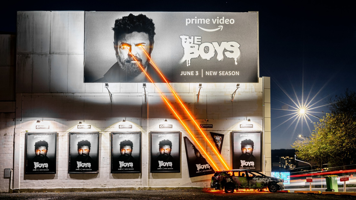a billboard depicting Billy Butcher from The Boys destroying a car parked below with his laser eyes